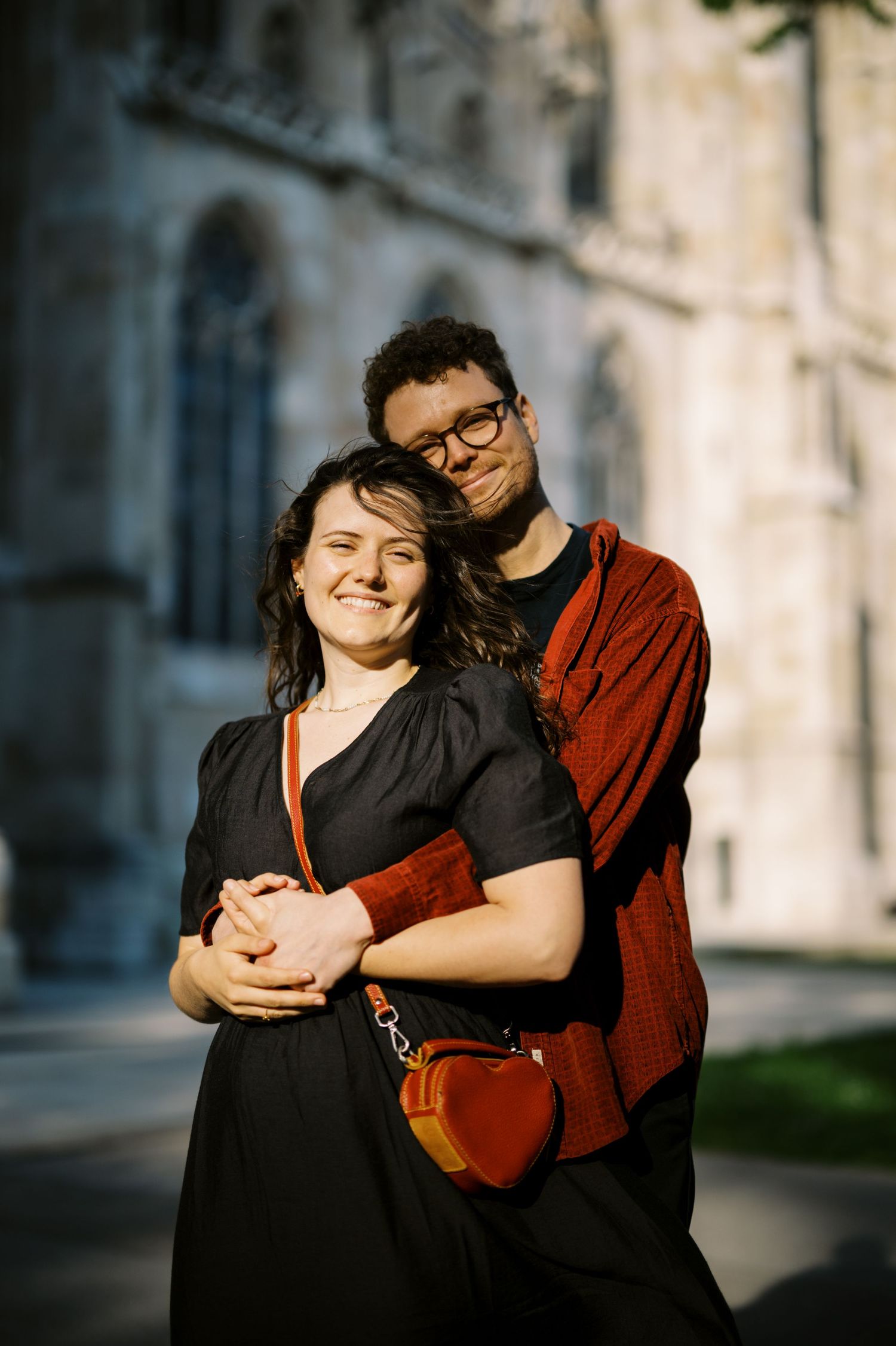 A couple embraces while standing outside a historic building on a sunny day.