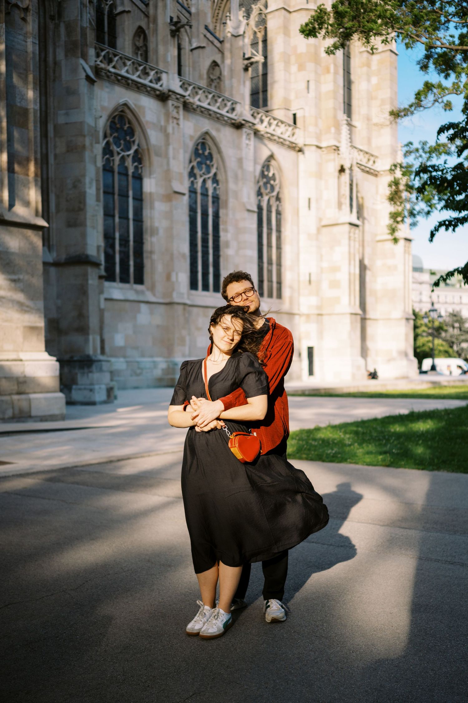 Couple embracing in front of a Gothic cathedral with ornate stone architecture and arched windows.