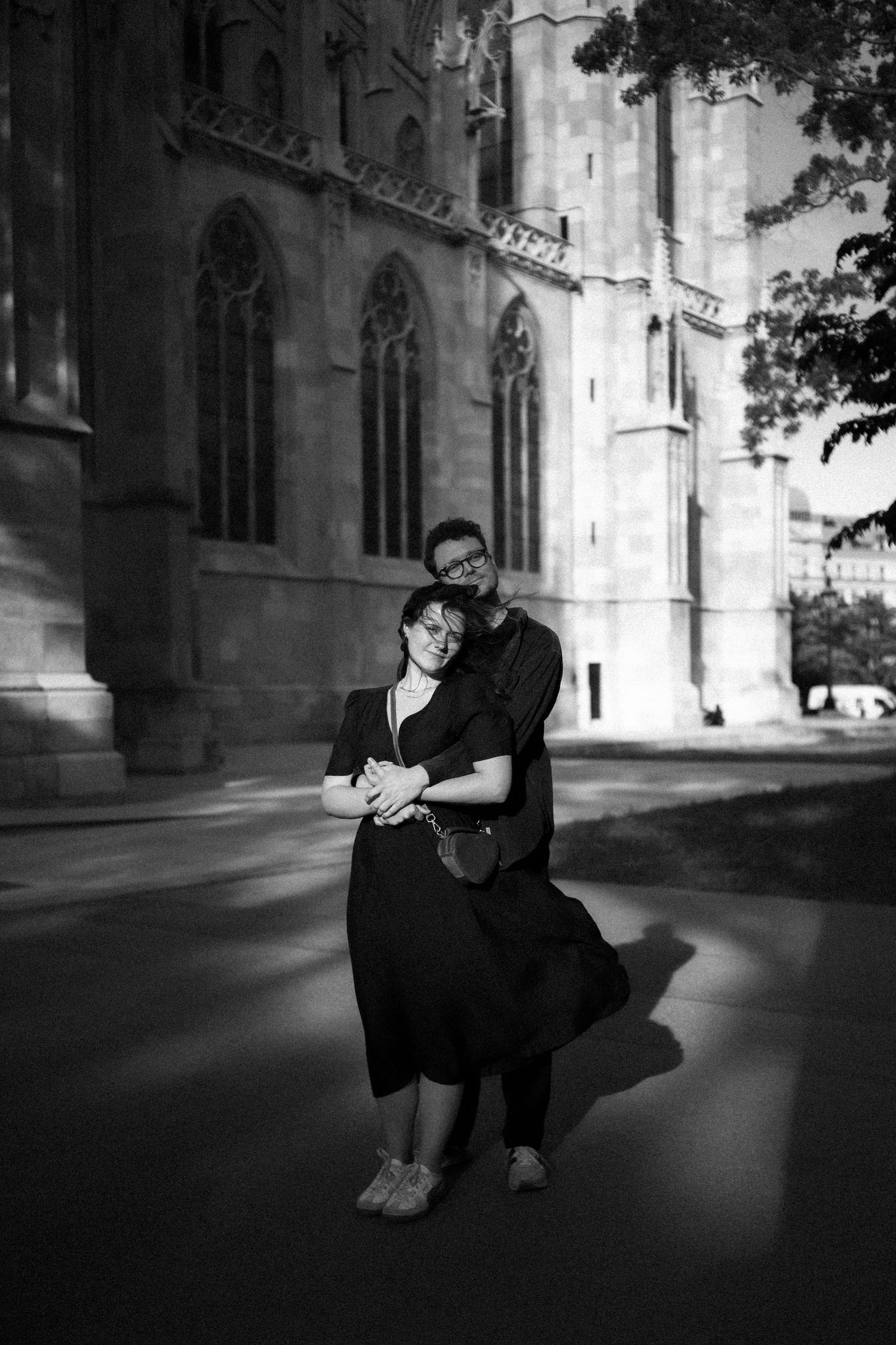A couple shares an intimate moment outside a gothic cathedral in black and white.