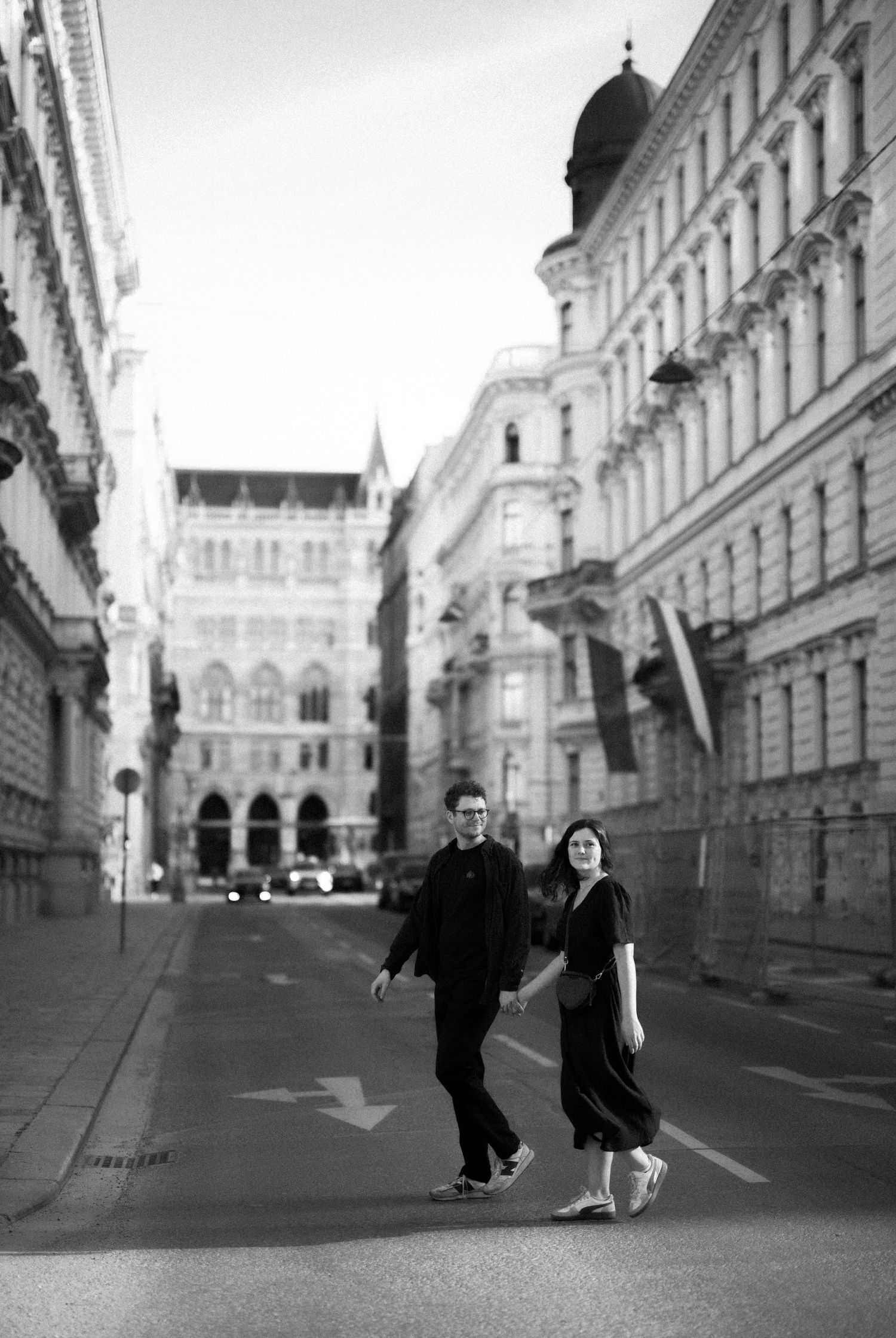 A couple poses elegantly on a historic European street with classic architecture in black and white.