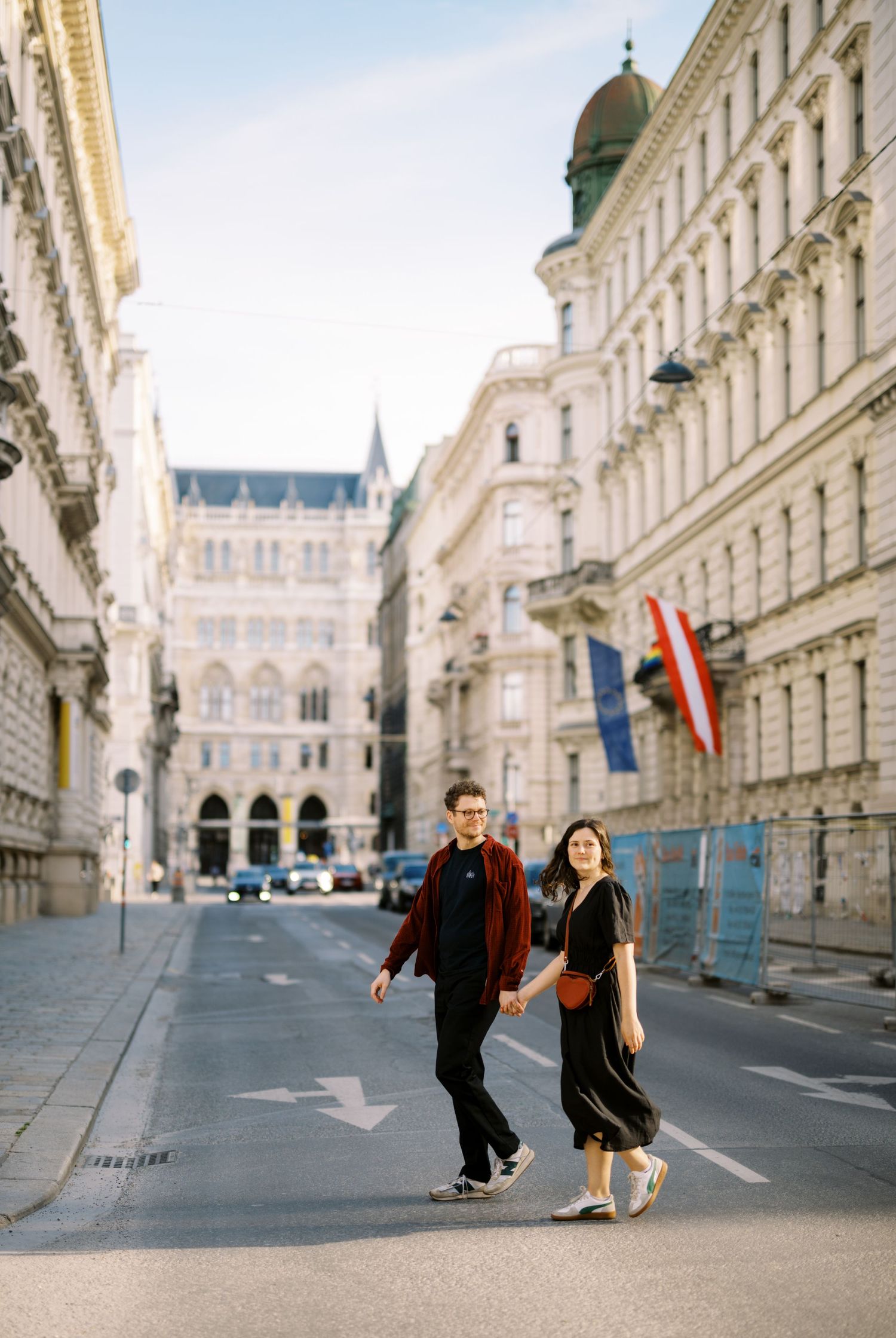 A couple strolls through Vienna's elegant streets with grand historic buildings and flags in the background.