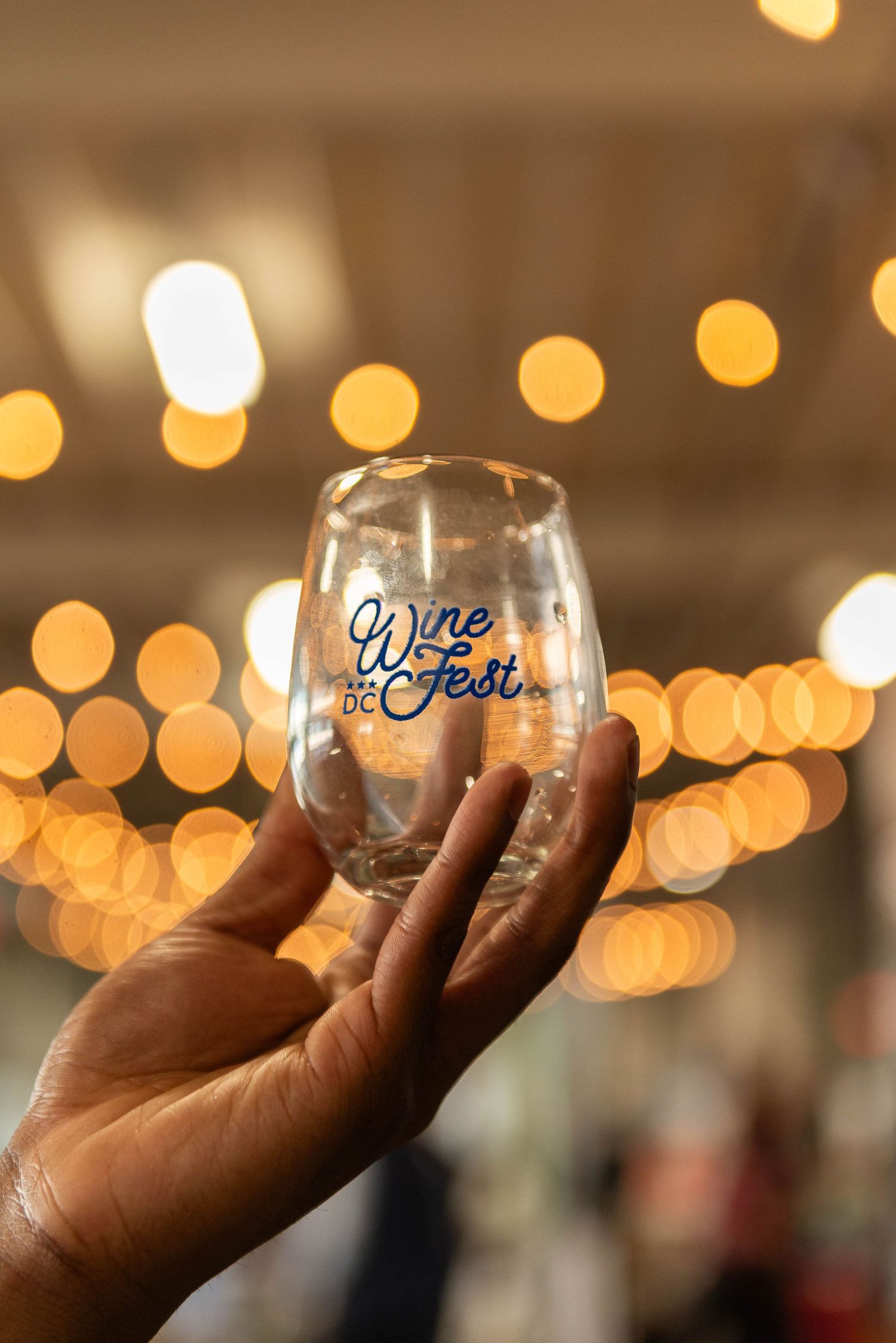 Wine glass held up against blurred golden bokeh lights background.
