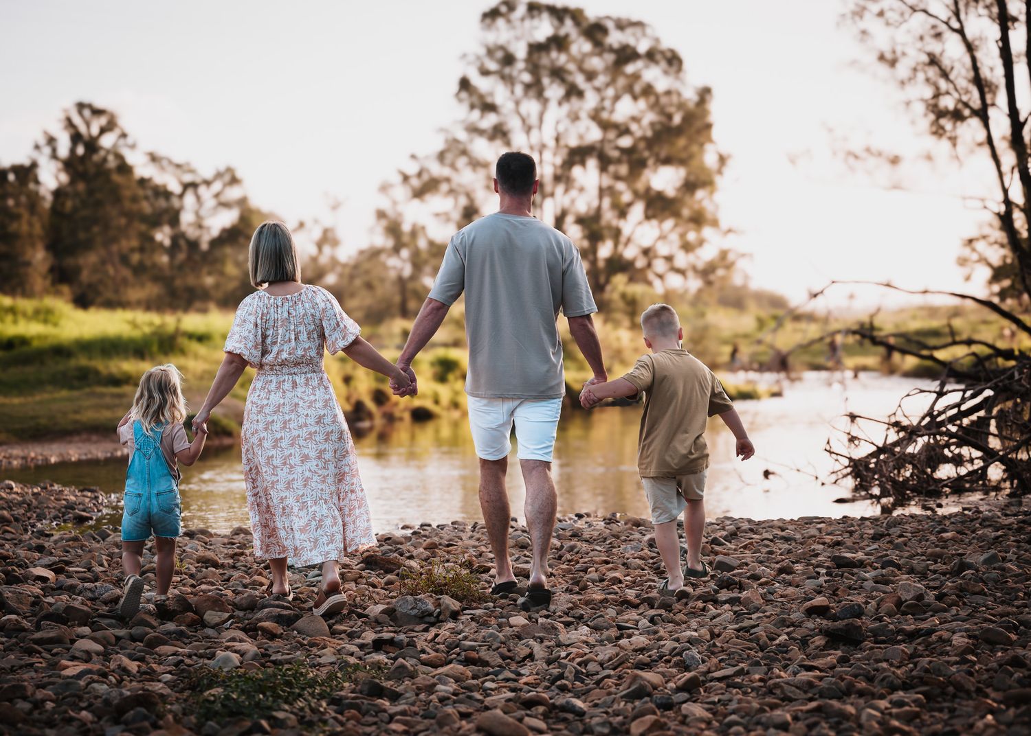 Family holding hands while walking along a riverbank at sunset.