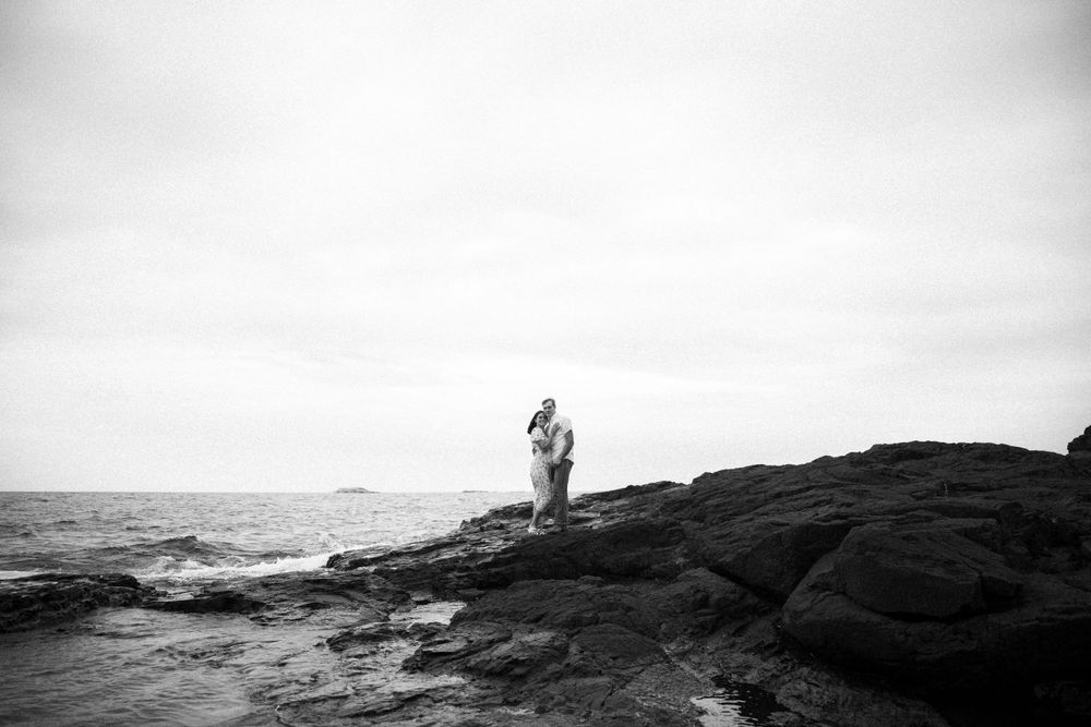 A silhouetted figure stands on dark rocky shore against a misty ocean backdrop captured in black and white.