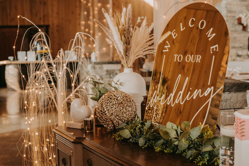 Rustic wooden wedding welcome sign with pampas grass and greenery decor at reception entrance.