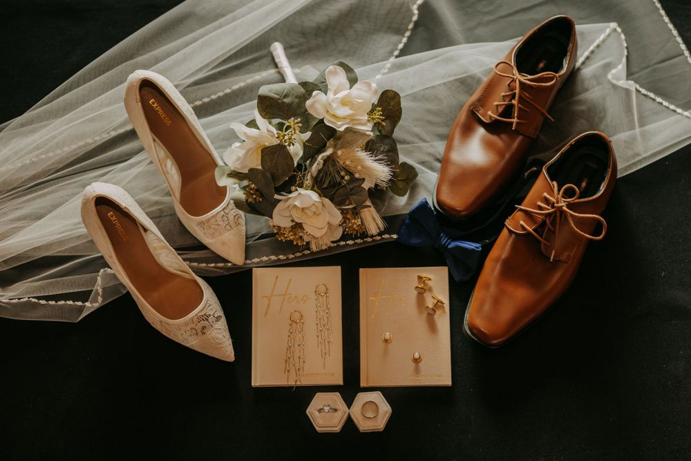 Wedding flat lay with brown leather shoes, white heels, and floral accessories.