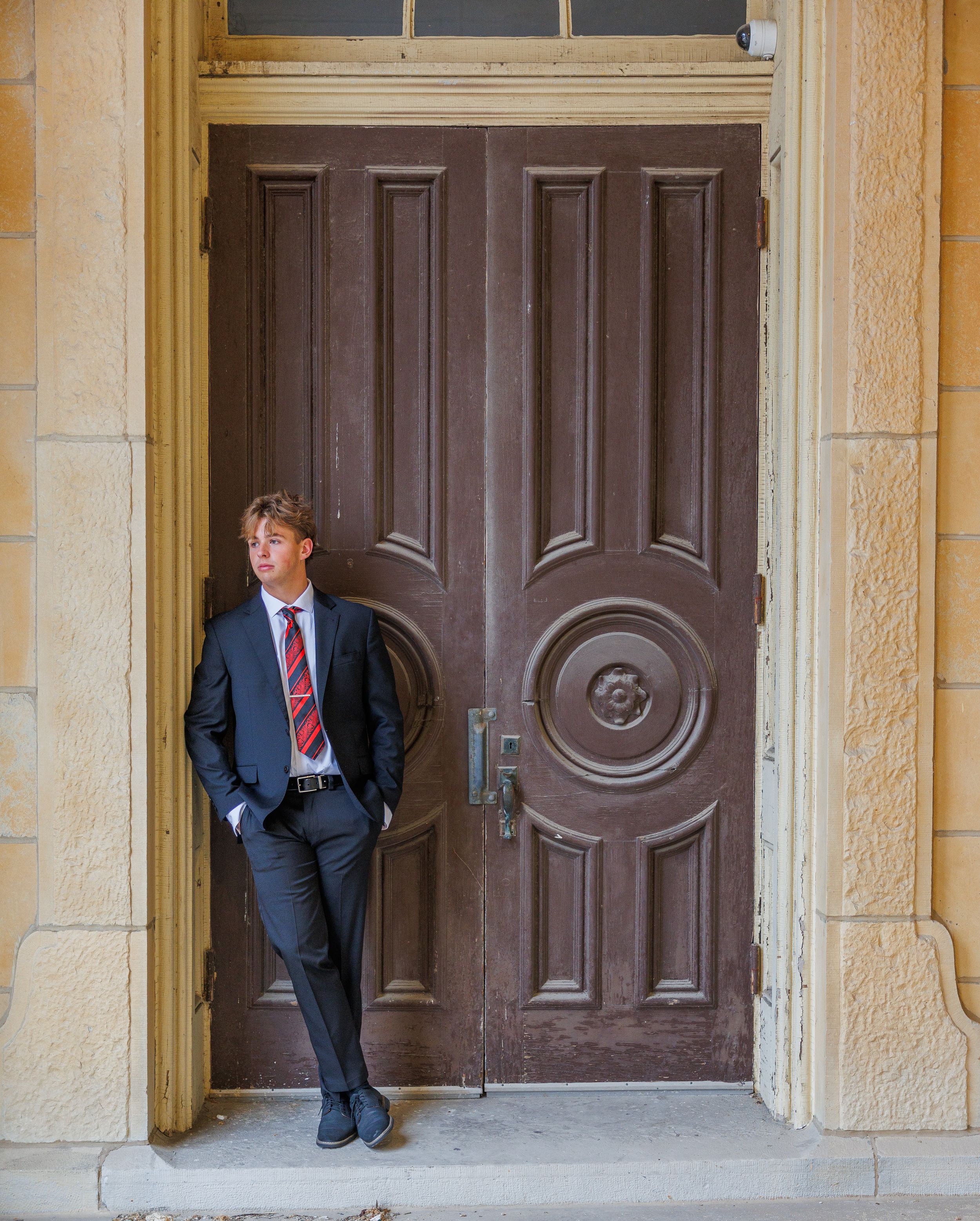 A person in a suit stands in an ornate doorway of a historic building with multiple wooden doors.