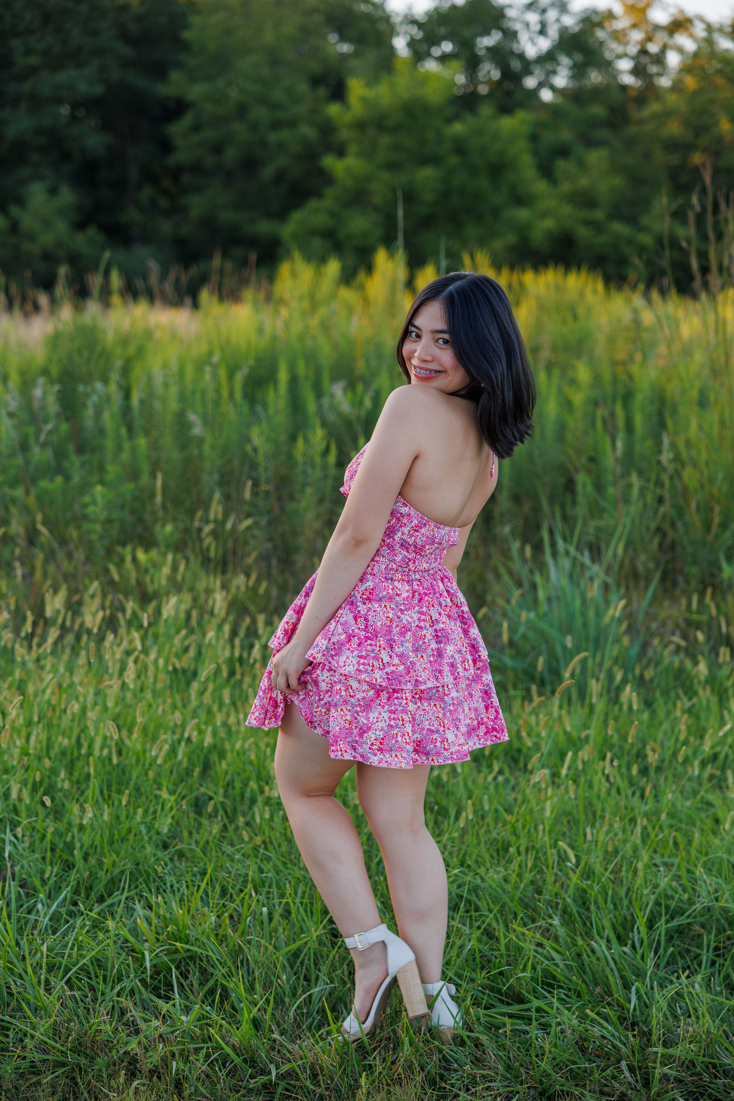 A person in a pink floral dress plays in a lush green meadow on a summer evening.