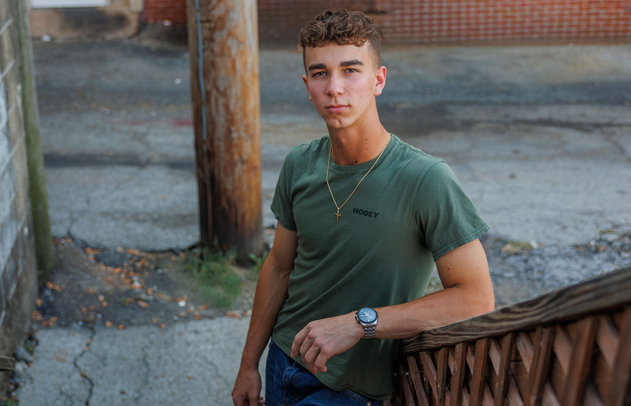 Young man in green t-shirt poses casually outdoors against urban background at dusk.