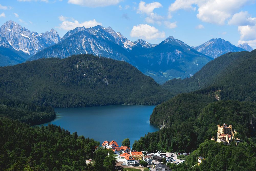Aerial view of Alpsee lake surrounded by Alpine mountains and lush green forests in Bavaria.