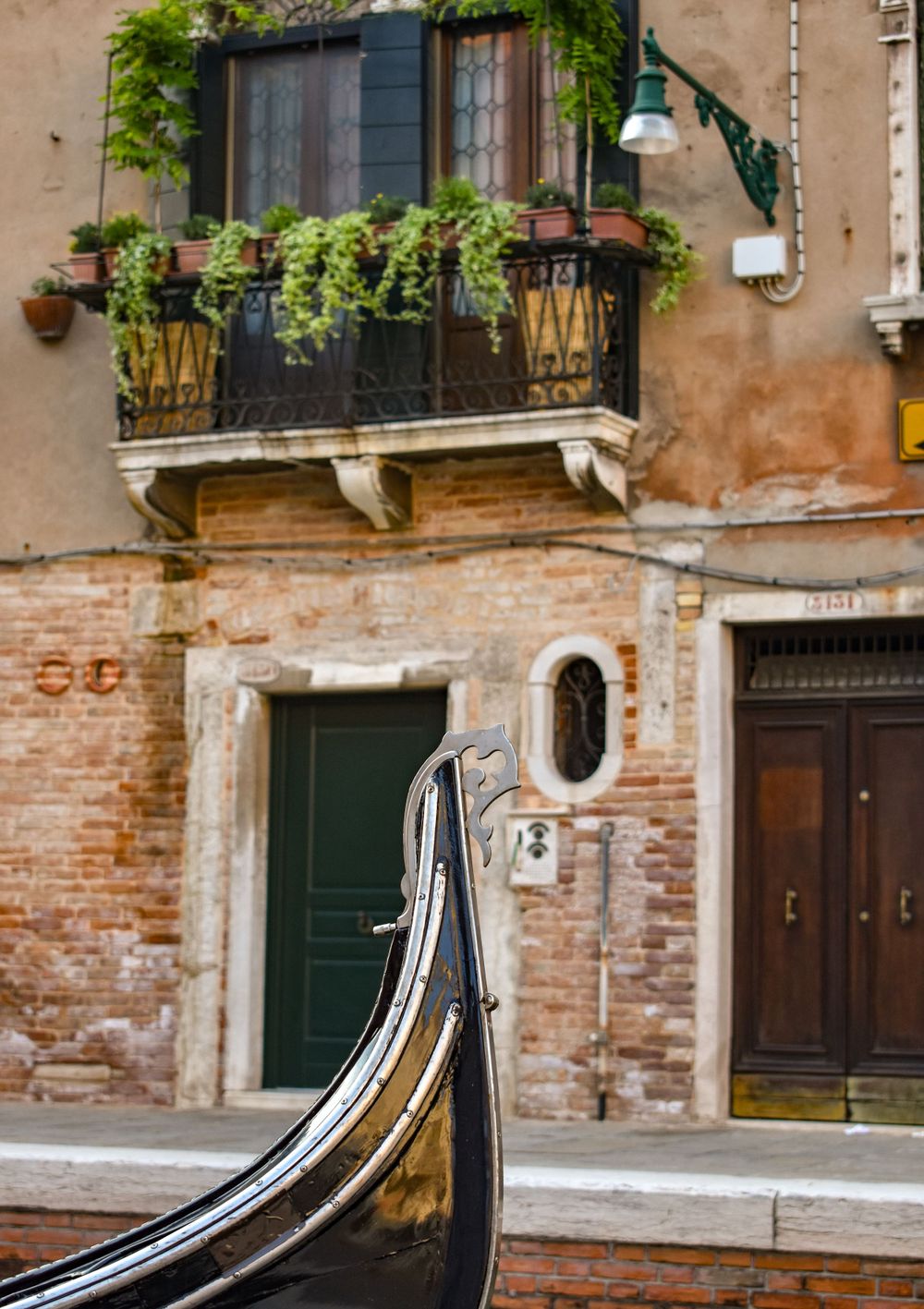 Front bow of a gondola docked by a rustic brick building with balcony in Venice, Italy.