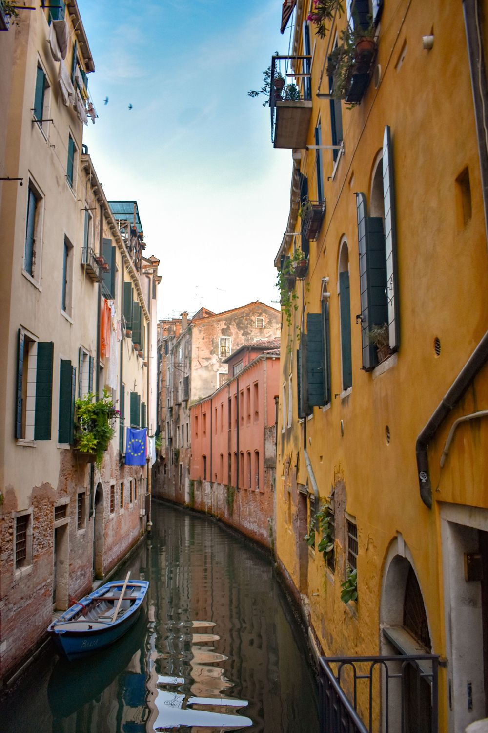 Narrow Venetian canal lined with colorful aged buildings and a moored boat in Venice, Italy.