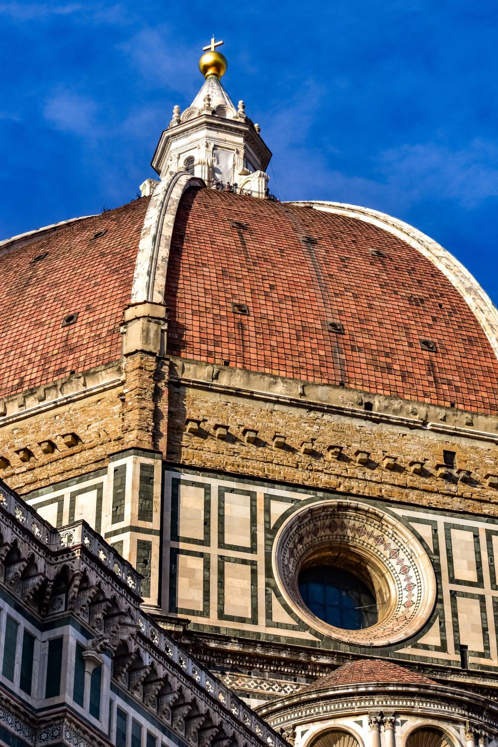 Close-up of Brunelleschi dome of Florence Cathedral with ornate marble details and golden cross against blue sky.