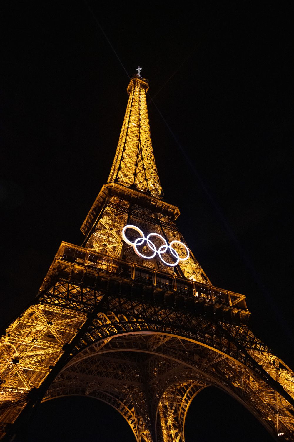 The Eiffel Tower illuminated at night displaying the Olympic rings symbol on its structure against a dark sky.