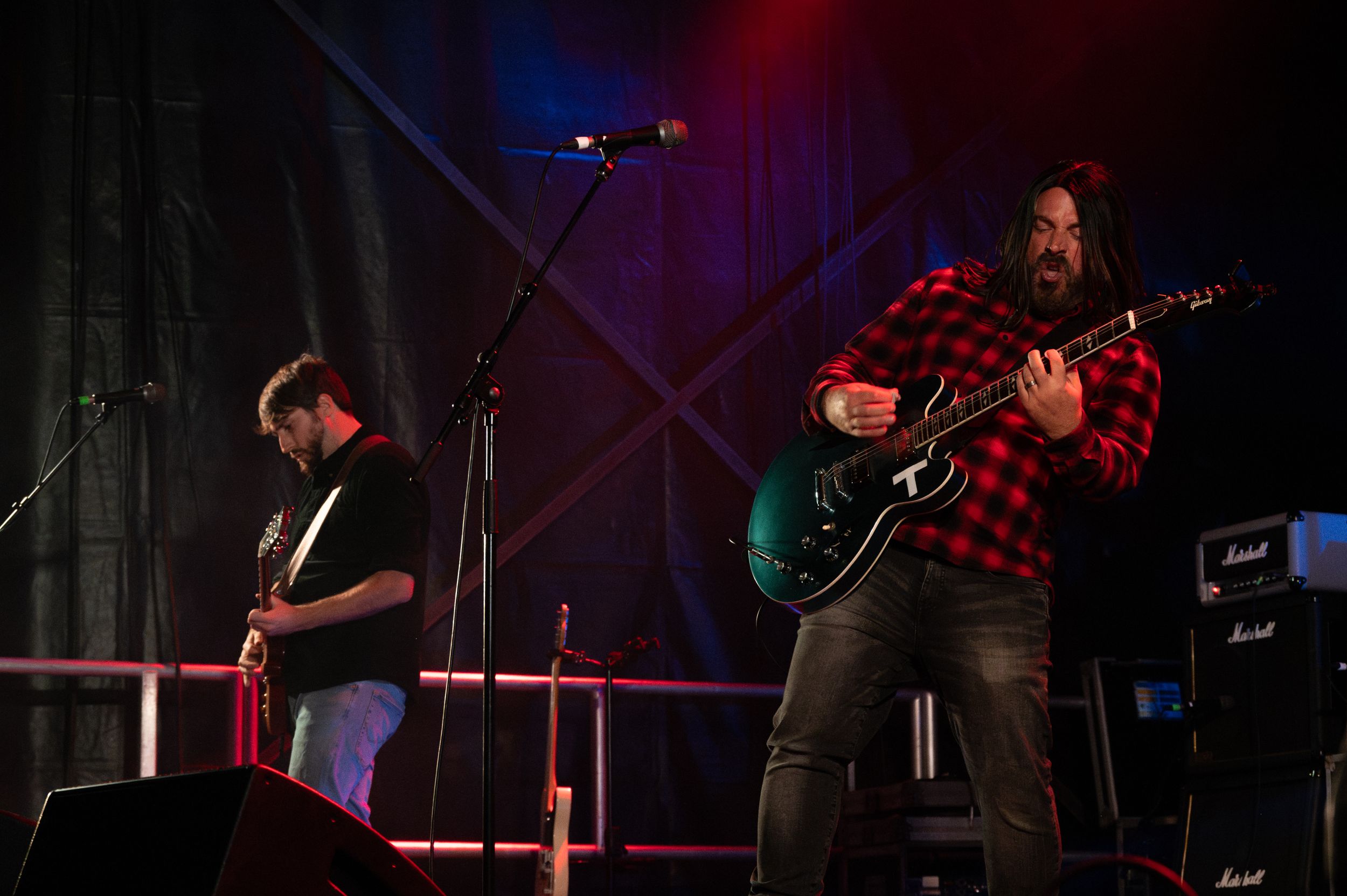 Two guitarists perform together on stage with dramatic concert lighting.