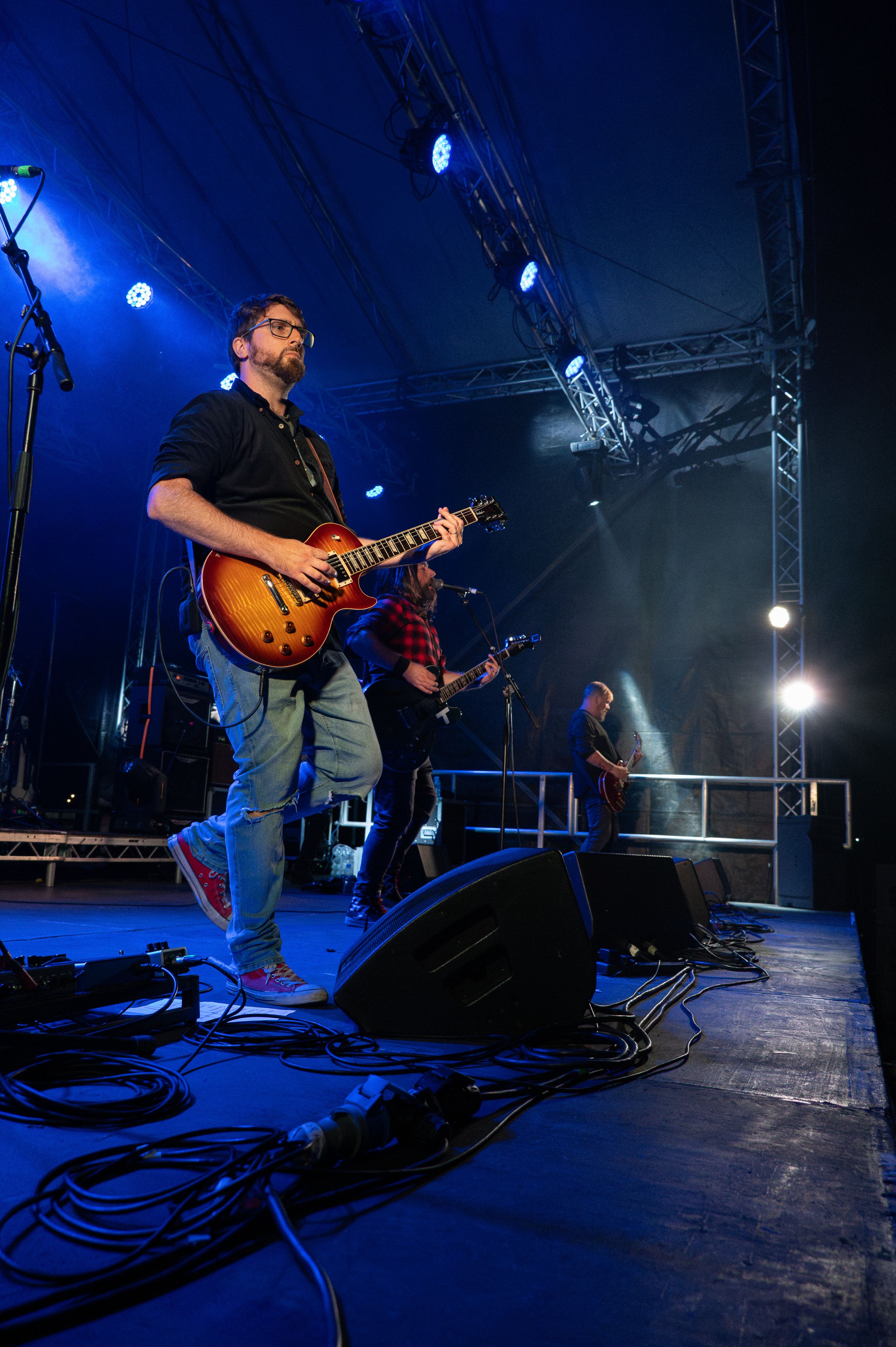 Musicians perform on elevated stage with dramatic blue lighting and equipment cables.
