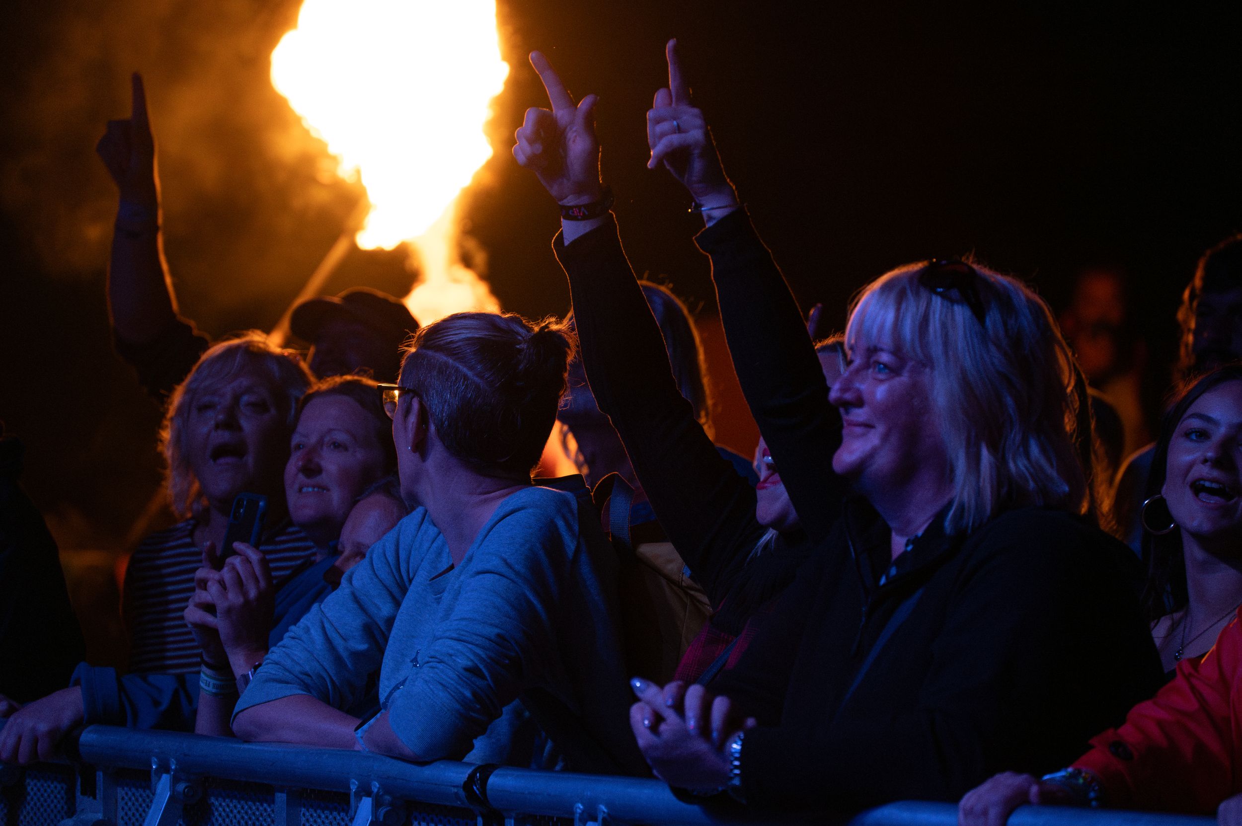 Concert crowd watches performance with bright flames illuminating the background.