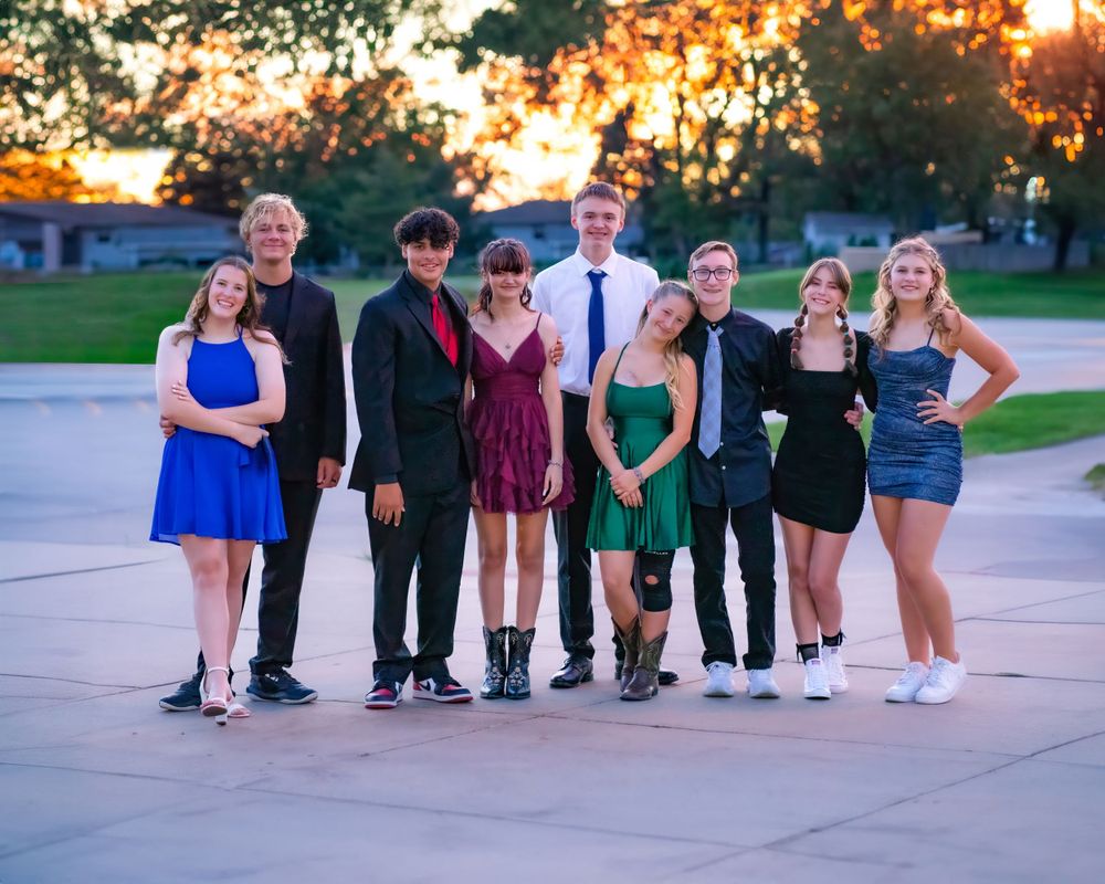 A group of students pose in formal attire at sunset during a school dance or prom event.