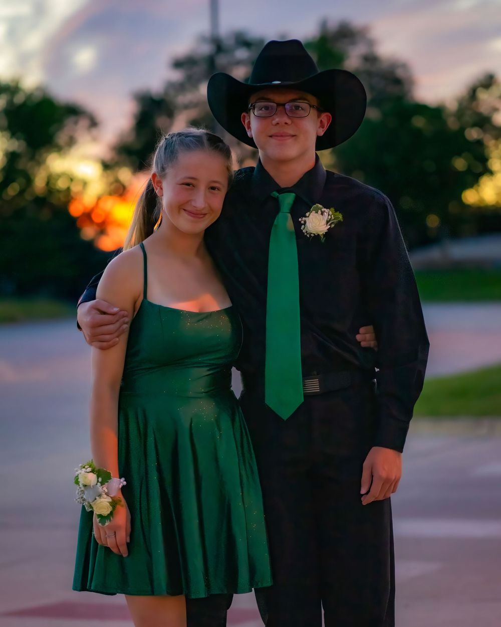 A couple poses at sunset wearing formal attire in black and emerald green for a special occasion.