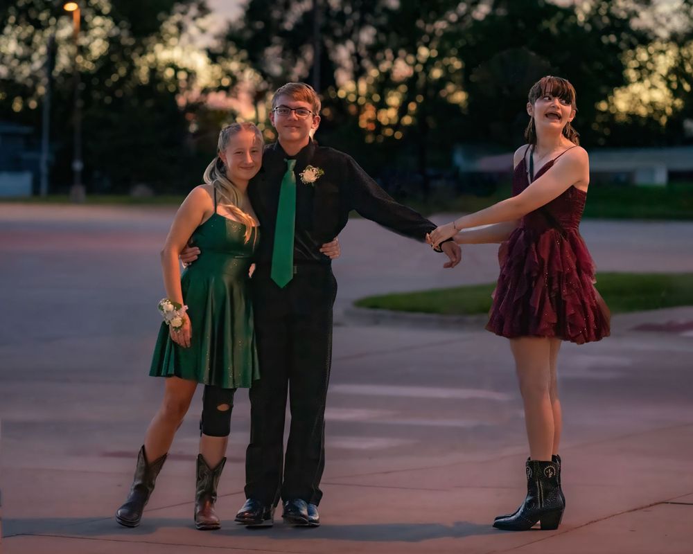 Three people in formal attire pose together at sunset during an outdoor event.