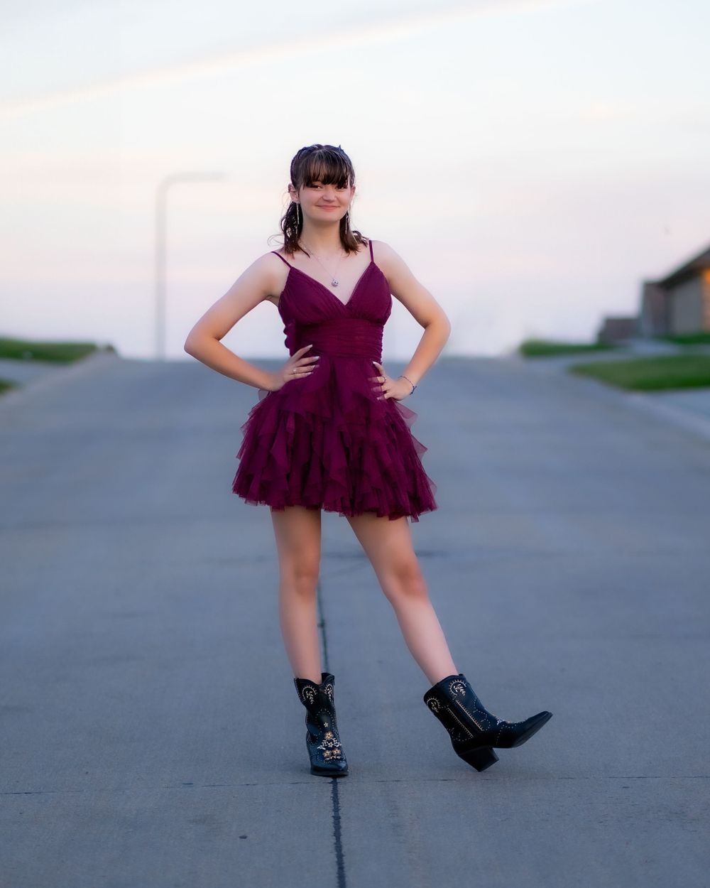 A stylish burgundy cocktail dress with tulle skirt is paired with black combat boots on a road at dusk.