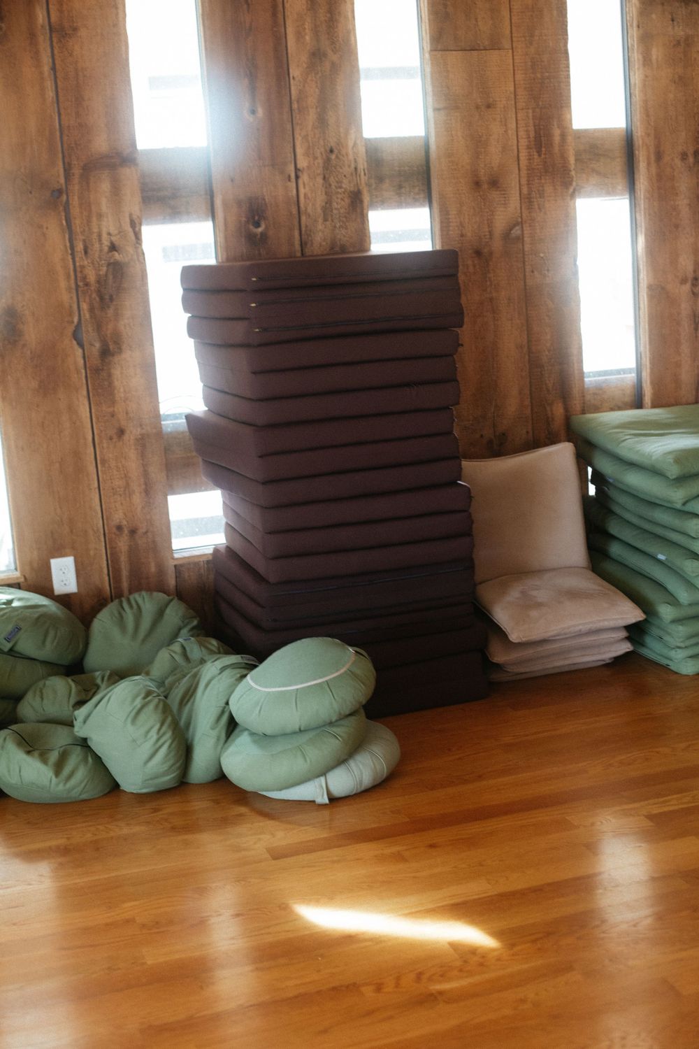 Detail photo of a stack of yoga mats and support pillows stacked together in front of a sunny wall in a community studio in Portland, Maine.