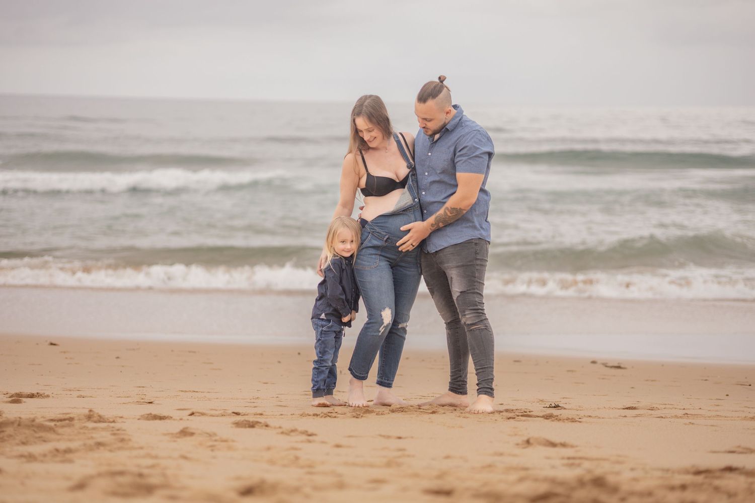 Happy family with young child plays on sandy beach with ocean waves in background.