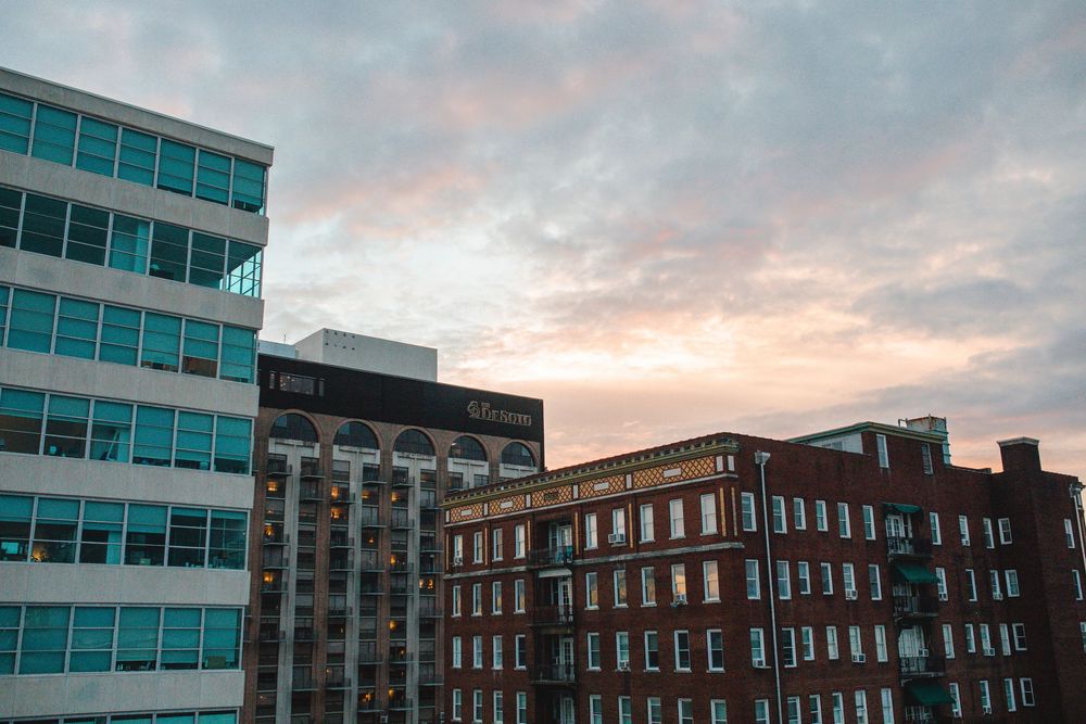 Urban skyline at dusk featuring modern glass and classic brick buildings under a dramatic cloudy sunset sky.