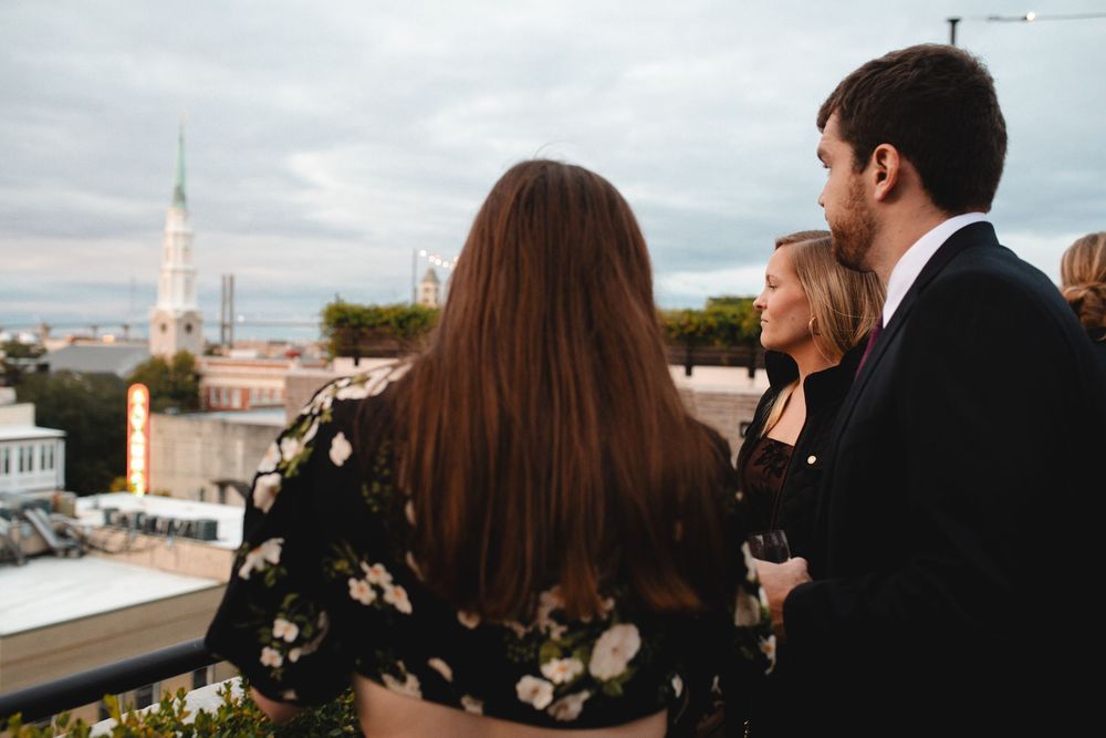 Three people on a rooftop terrace admiring city skyline views at dusk with a church steeple in background.