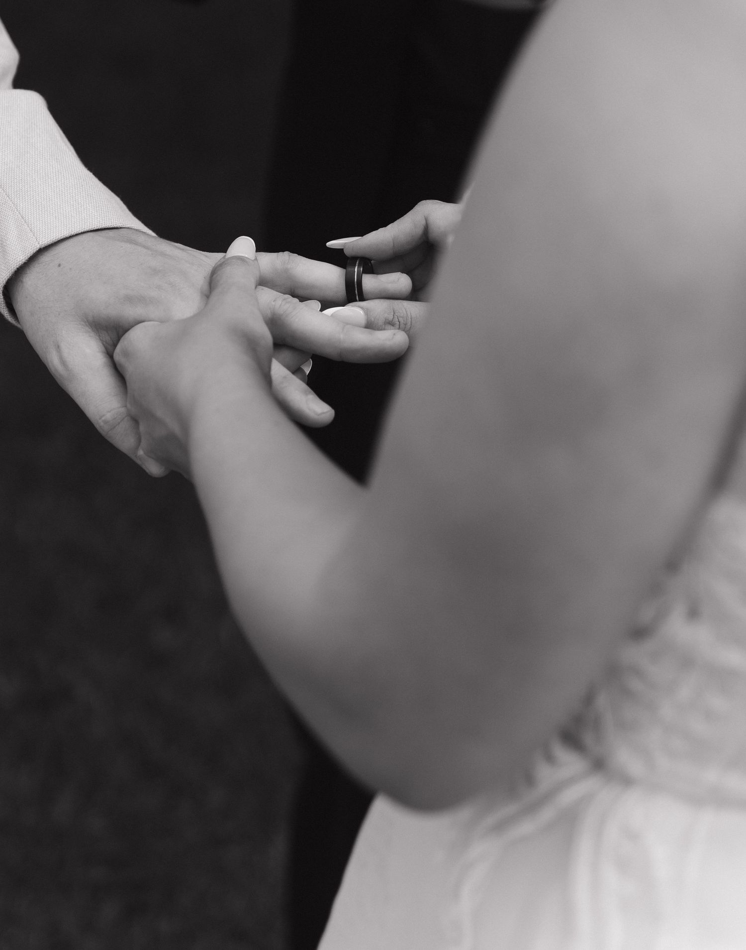 Black and white photo of a groom placing a wedding ring on the bride's finger during a wedding ceremony.