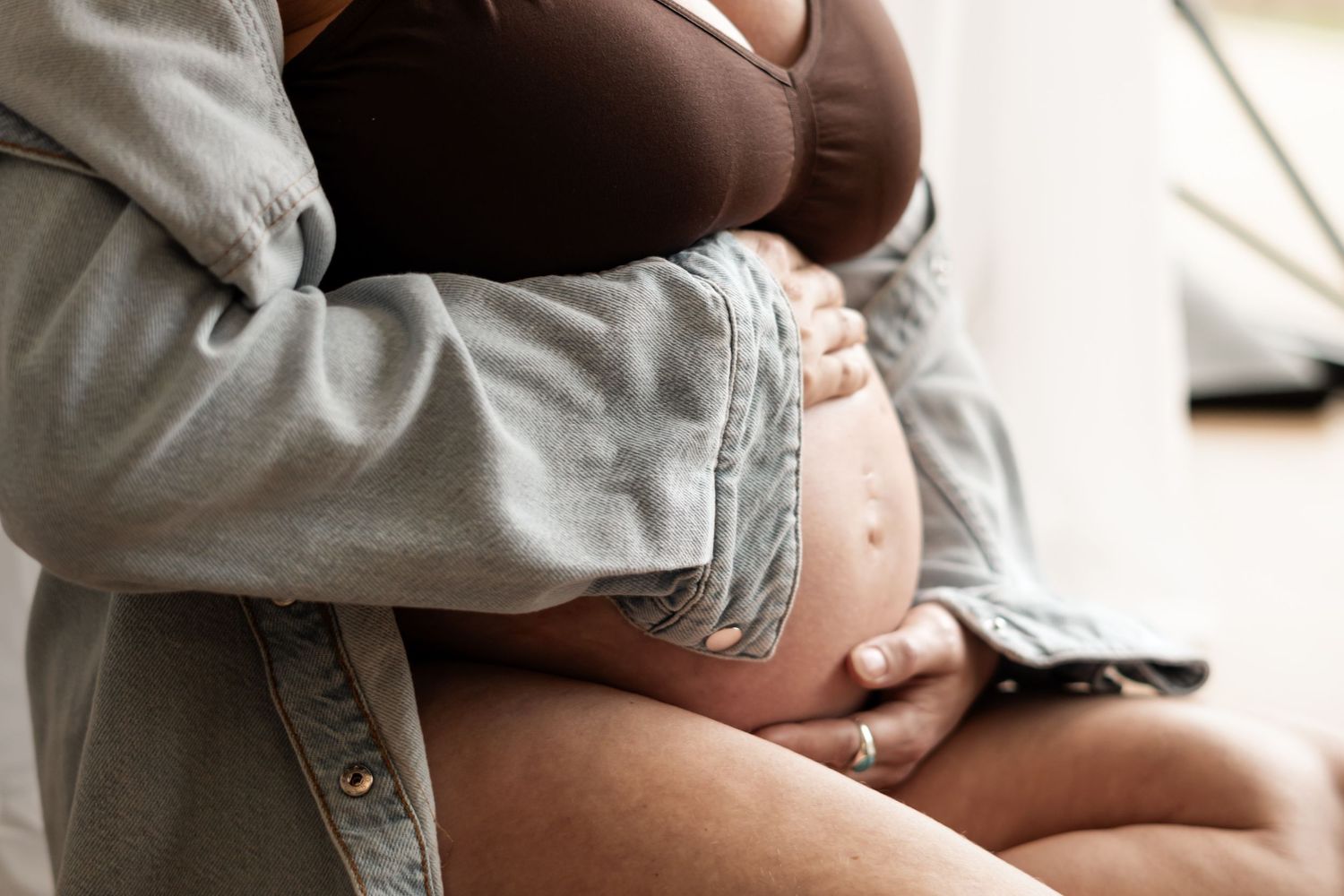 Couple embracing pregnant woman's bare baby bump, maternity photography closeup shot.