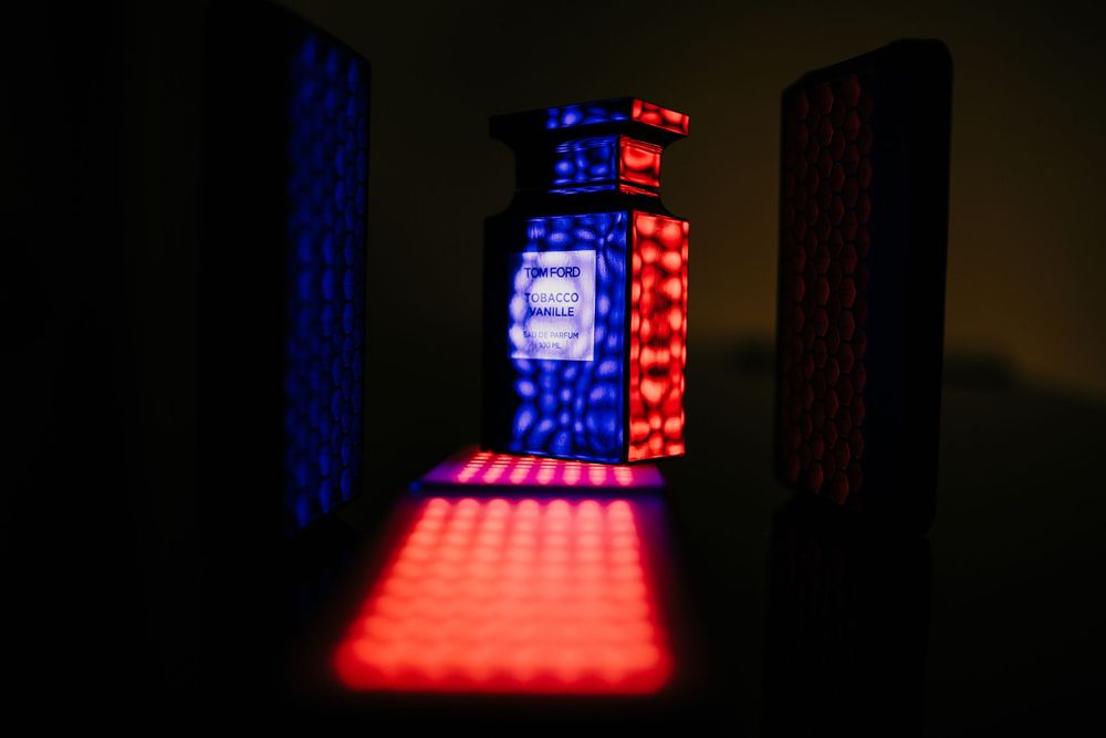 Artistic perfume bottle illuminated by red and blue LED lights in dramatic dark setting.