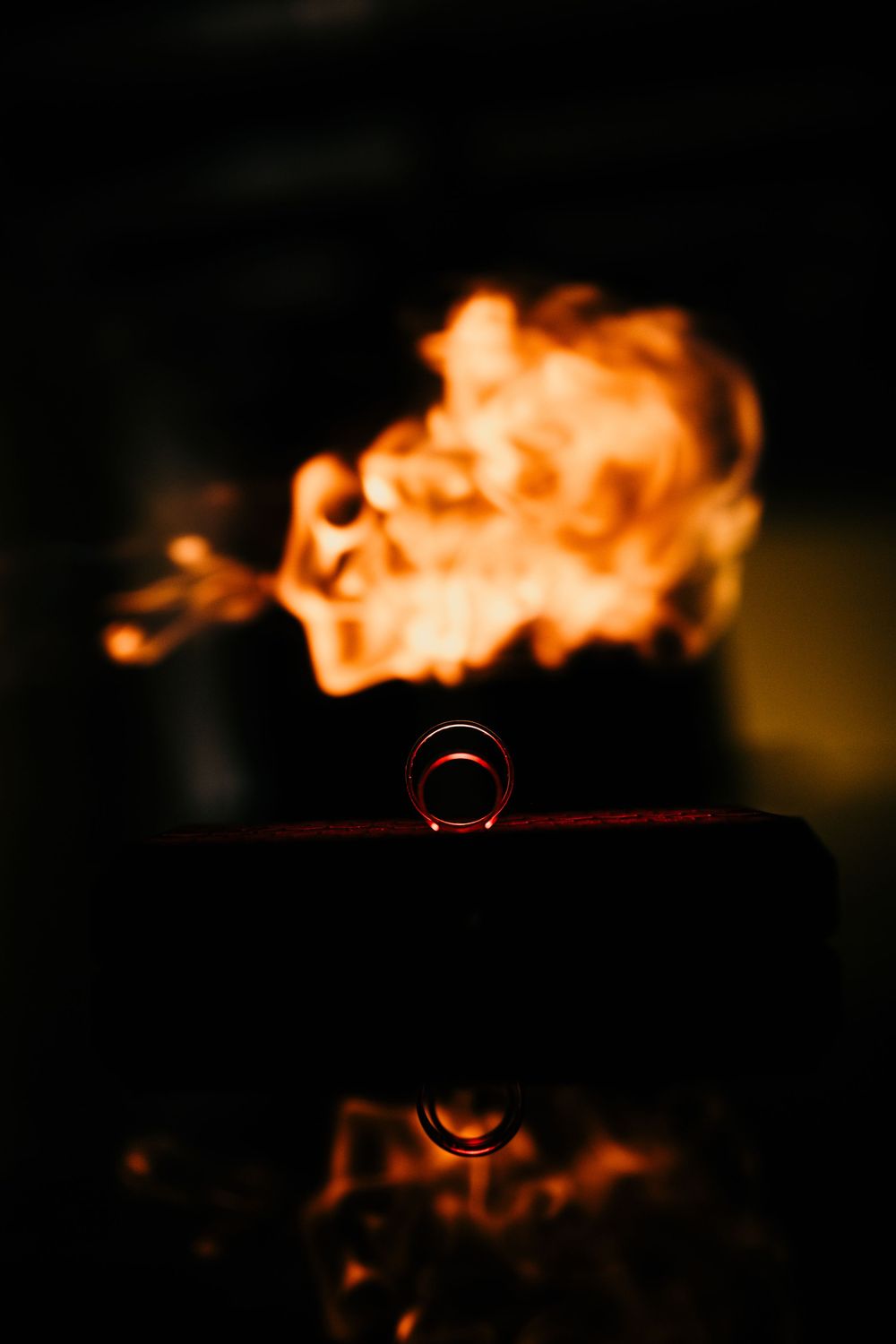 Single wedding band balanced on edge with dramatic fire flames glowing in background.