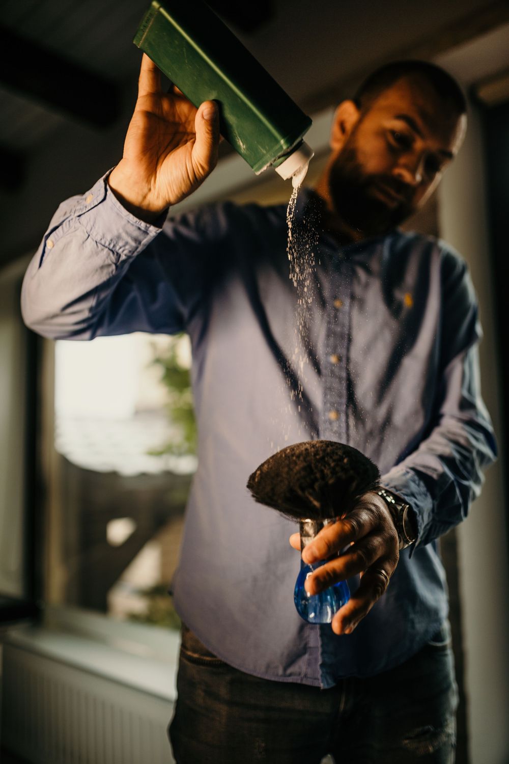 Barber pouring powder from green container onto brush preparing for grooming service.