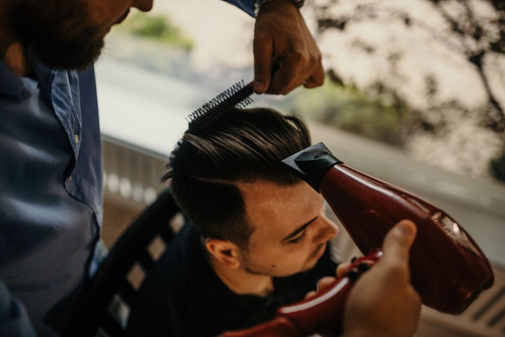 Barber styling a man's hair with a comb at an outdoor barbershop.