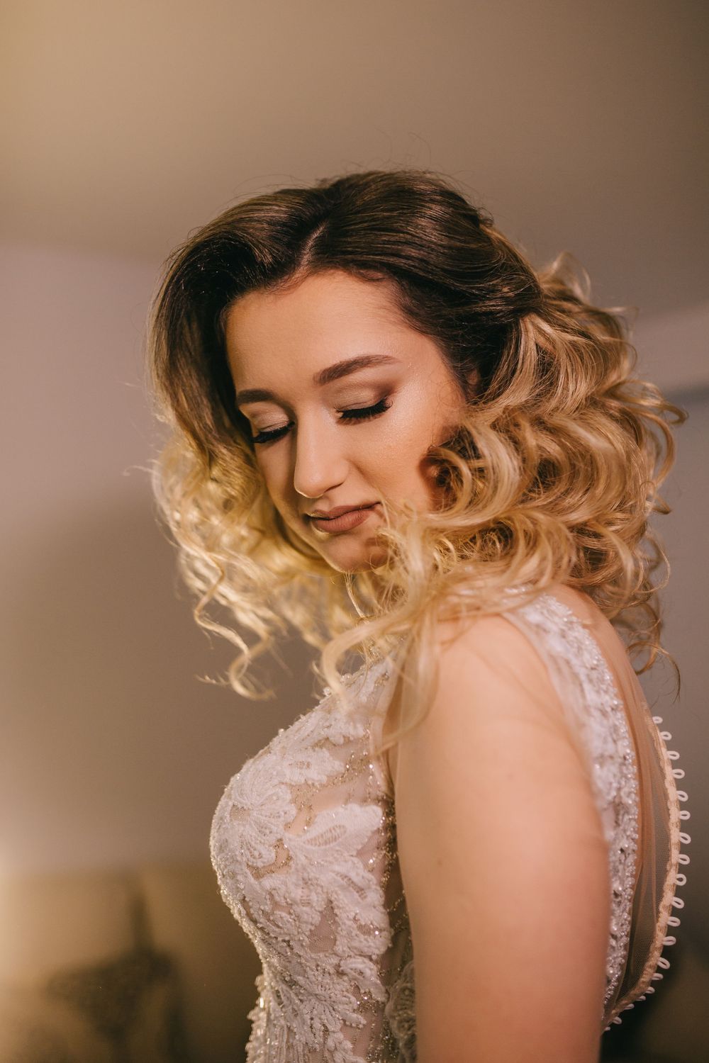 Beautiful bride with curly blonde ombre hair in elegant lace wedding dress.