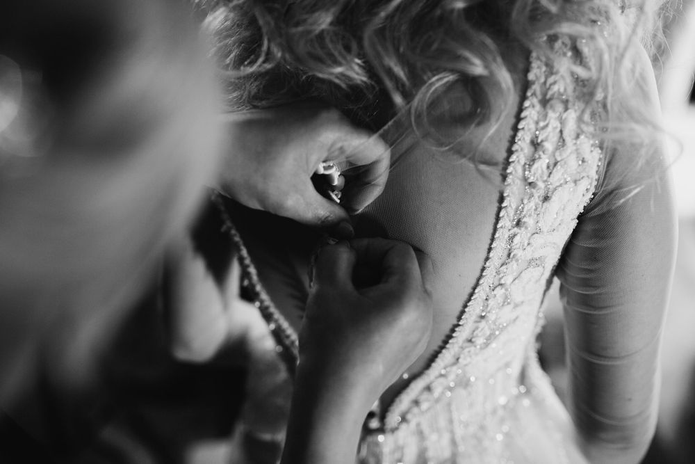 Black and white close-up of bride having wedding dress buttons fastened.