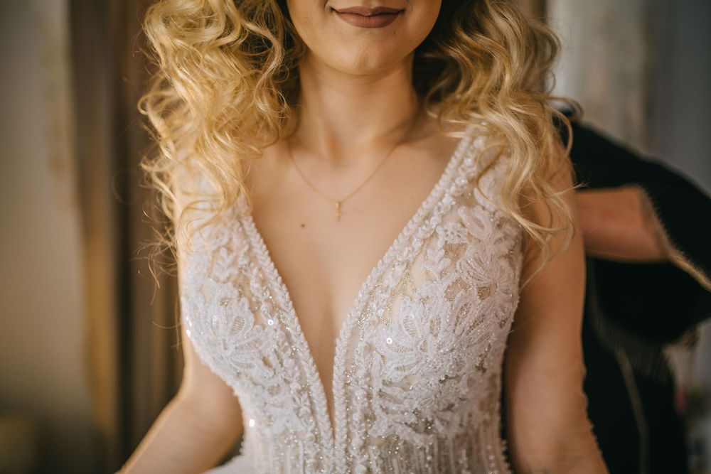 Bride in a beaded lace deep V-neck wedding gown with delicate necklace.