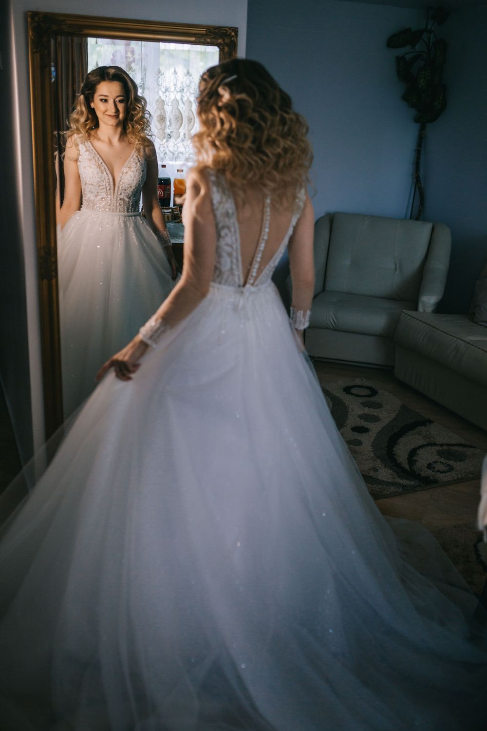 Bride in a white ballgown with lace back admiring her reflection in a mirror.