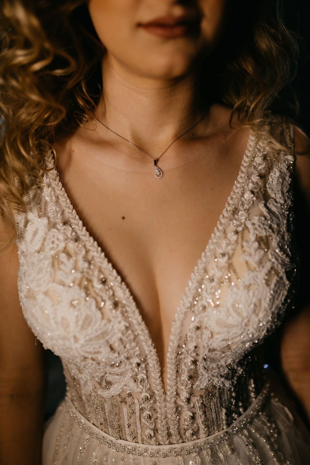 Close-up of bride in a sparkling beaded V-neck wedding dress with a delicate necklace.