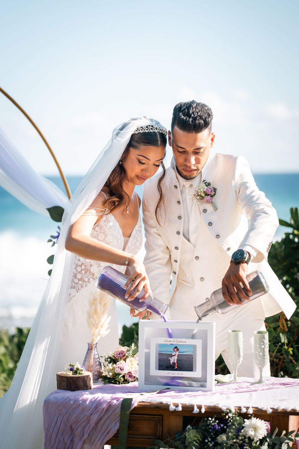 Bride and groom pouring sand during a beach wedding unity ceremony with ocean backdrop.