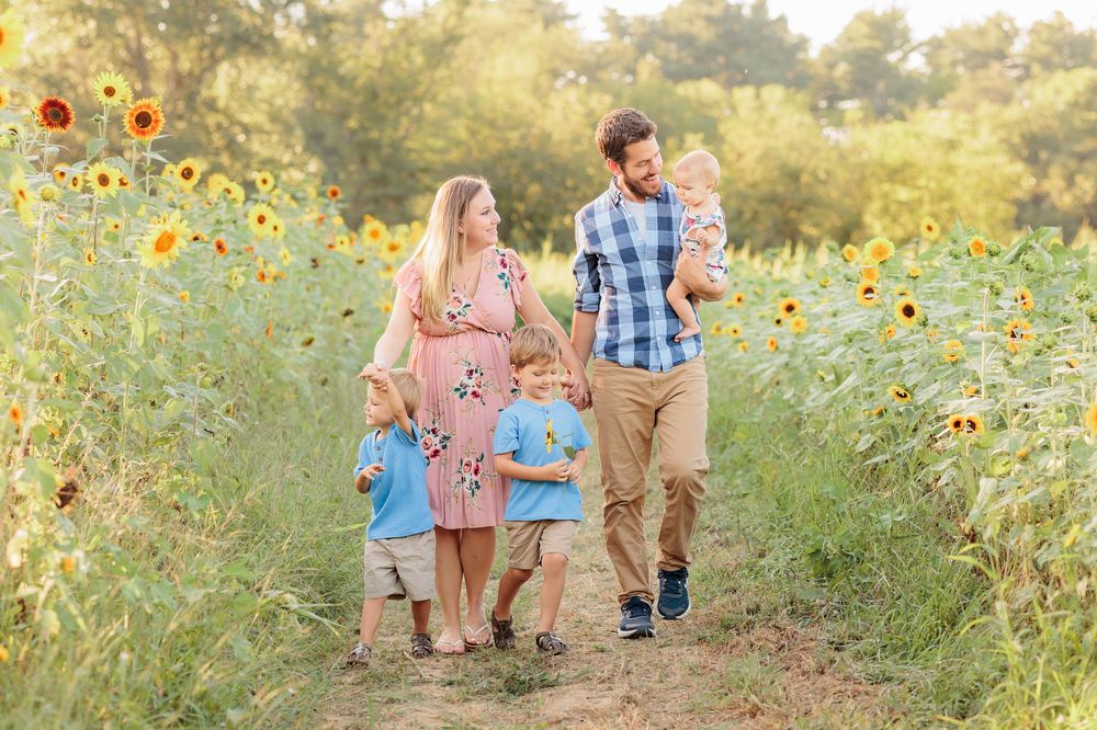Family walking through sunflower field, parents with three young children on sunny day.