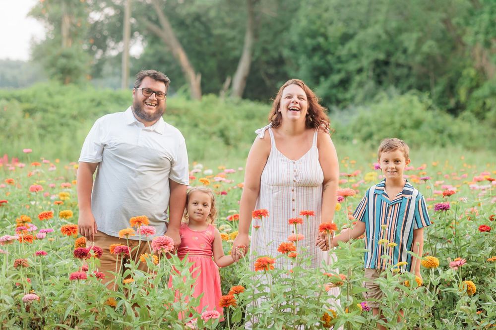Happy family of four laughing together in a vibrant orange zinnia flower field outdoors.