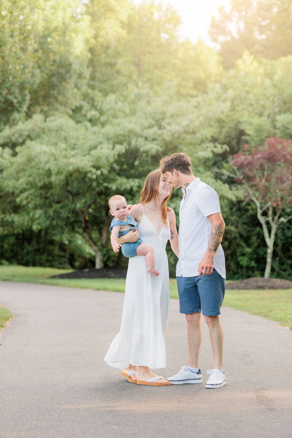 Young couple sharing a tender moment outdoors, holding their baby in a sunny park setting.