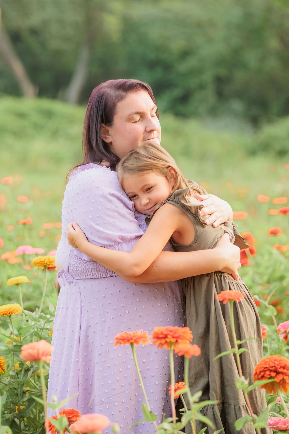 A mother and daughter share a warm embrace in a vibrant flower field with colorful zinnias blooming around them.