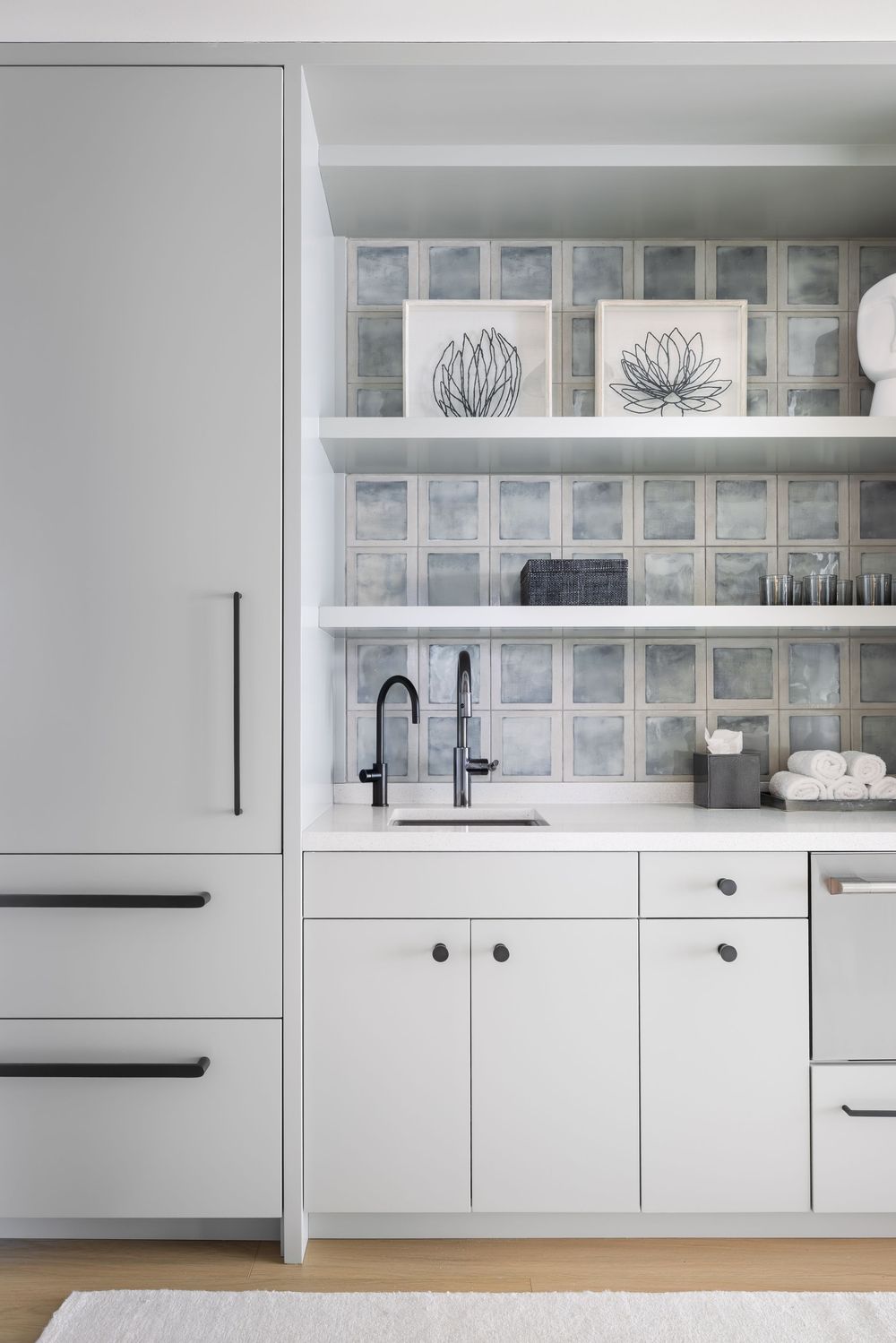 Minimalist white butler pantry with glass tile backsplash, open shelves, black hardware, and integrated refrigerator.