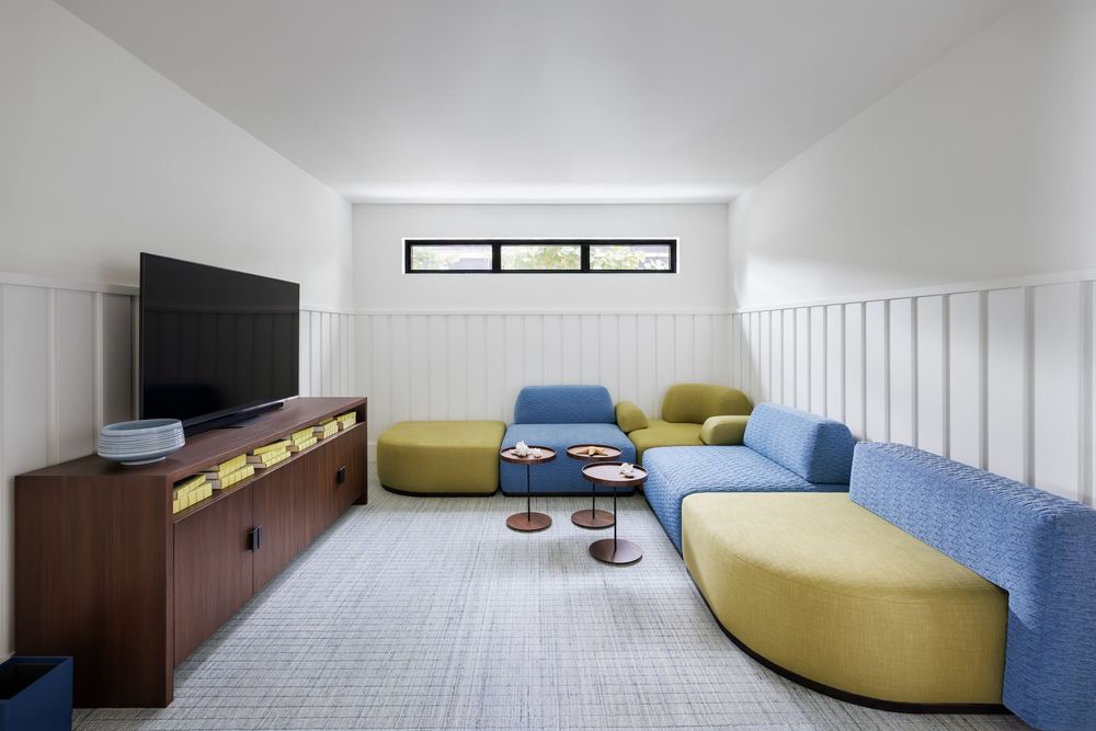 Modern media room with colorful modular blue and yellow-green seating, wall-mounted TV, and wood credenza.