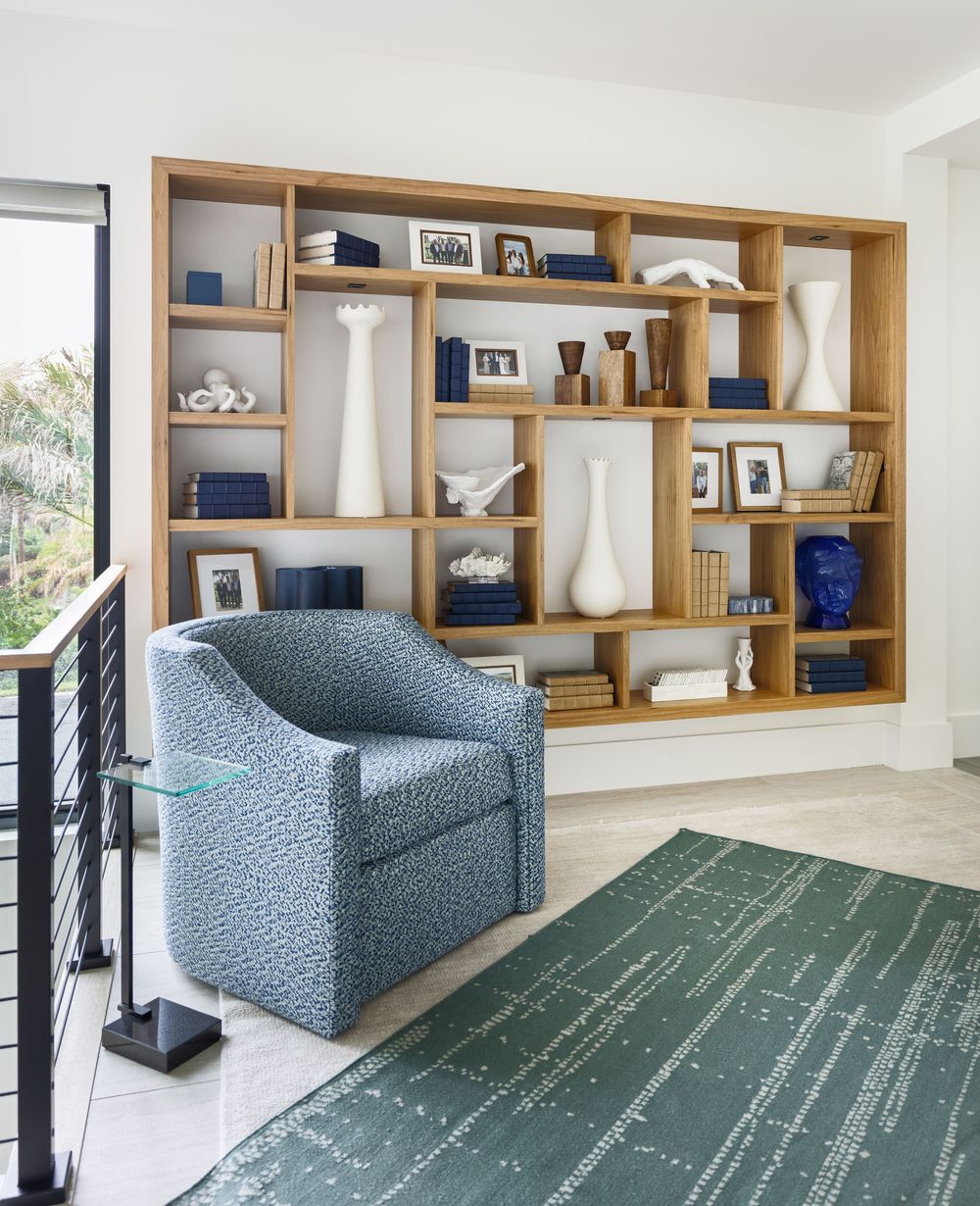 Built-in oak bookshelf styled with white vases and books beside a blue patterned accent chair and teal rug.