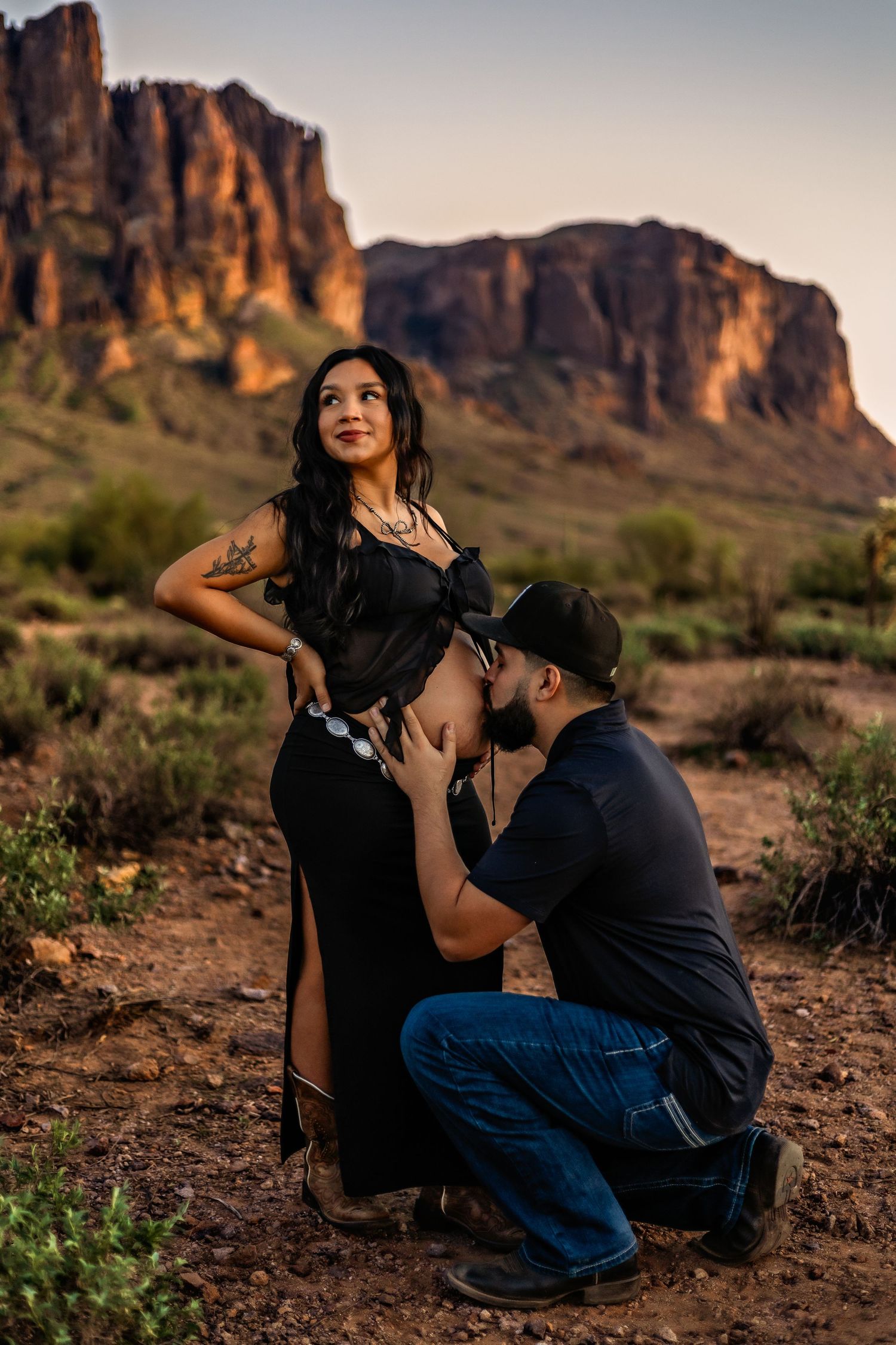 Maternity photo shoot at Superstition Mountains, Arizona, with couple in black outfits at golden hour.
