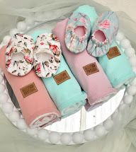 Pastel pink and mint baby gift set with floral booties and rolled swaddle blankets arranged on a white tray.